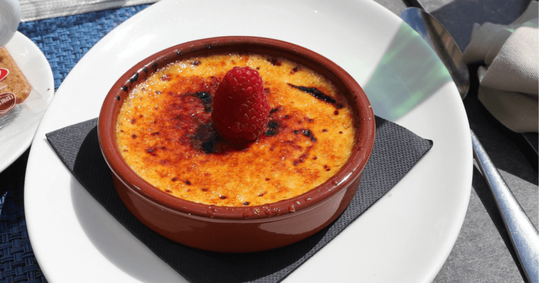A rich and creamy Crab Brulee Recipe brûlée with a caramelized golden crust, served in an elegant white ramekin on a dark surface.