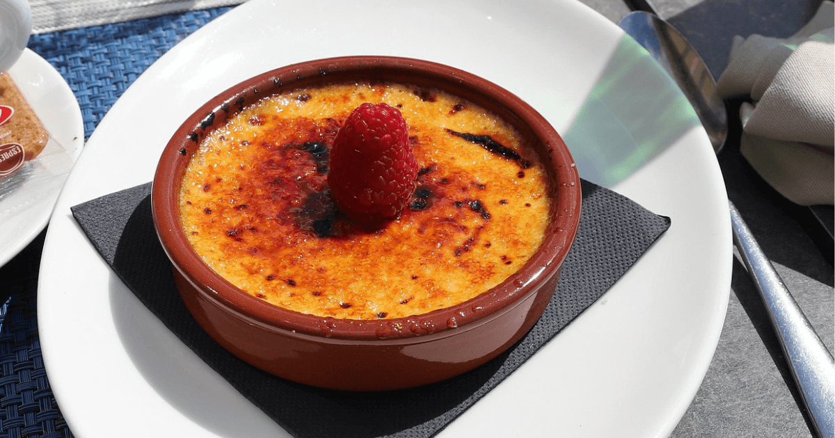 A rich and creamy Crab Brulee Recipe brûlée with a caramelized golden crust, served in an elegant white ramekin on a dark surface.